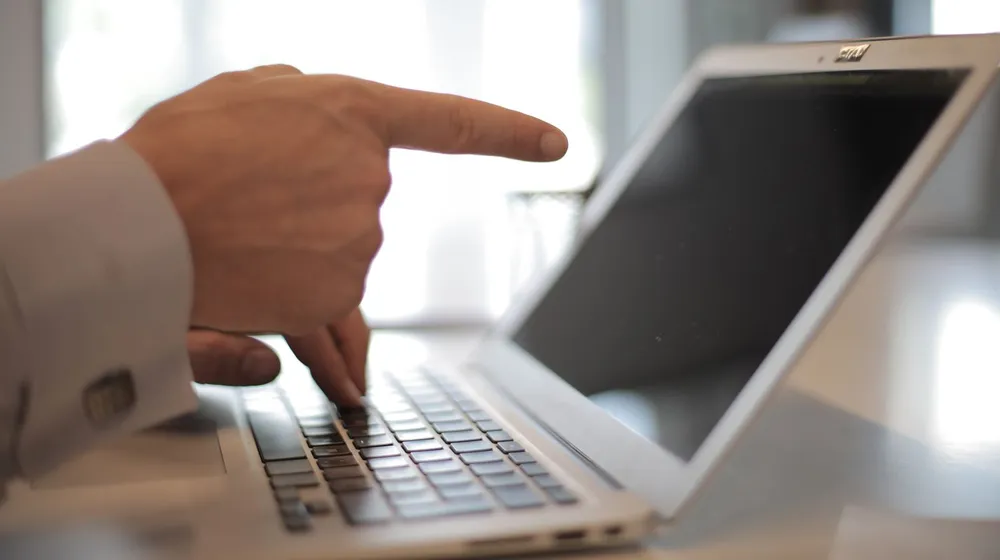 A hand pointing directly at a laptop screen, showing visitors exactly where to take the next action