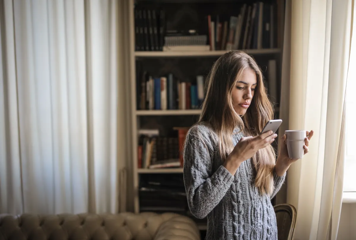 A customer reading a message on her phone with coffee, representing Klaviyo SMS flows