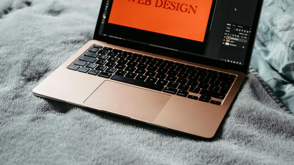 A laptop on a blanket showing a web design app — the casual, do-it-yourself approach