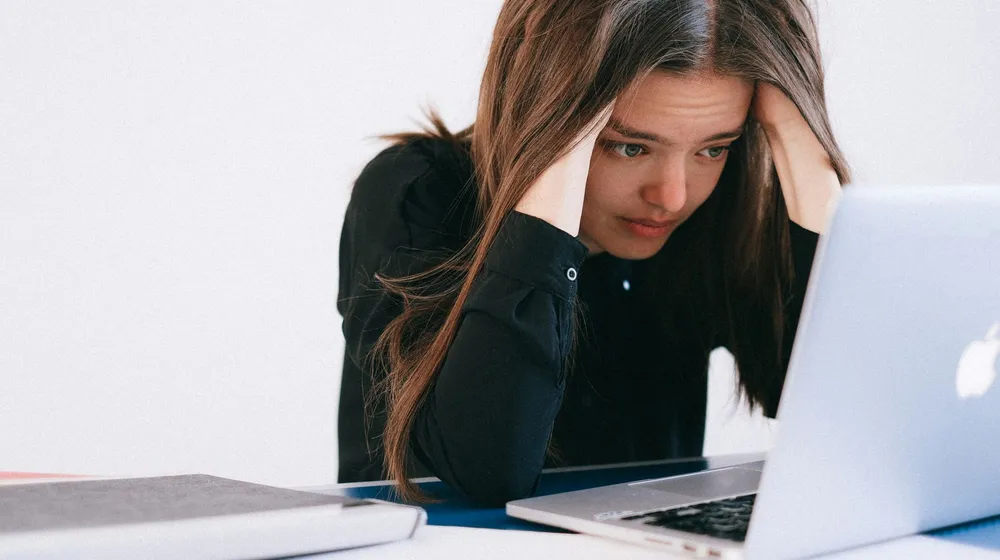 A frustrated business owner holding her head at her laptop after losing leads to follow-up mistakes