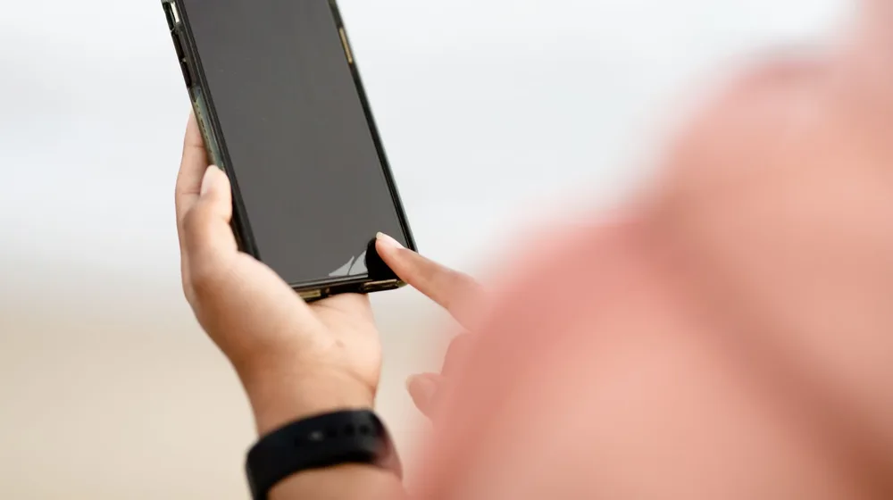 A person using a smartphone outdoors, tapping the touchscreen