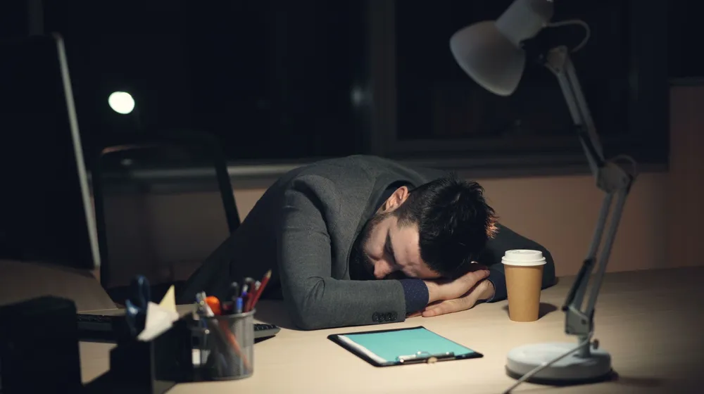 An exhausted business owner slumped at their desk late at night, too busy to follow up on new leads