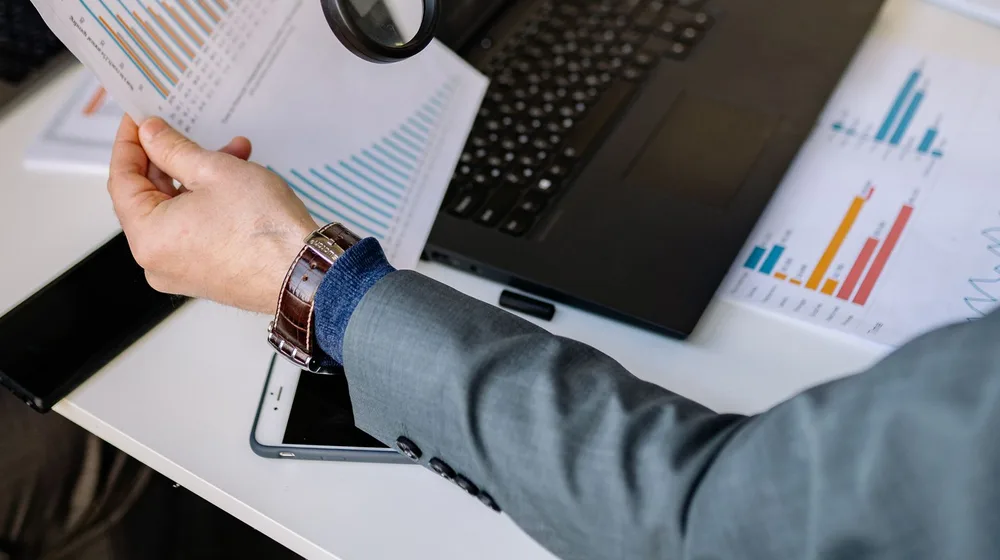 A magnifying glass over a laptop examining data charts — auditing website speed